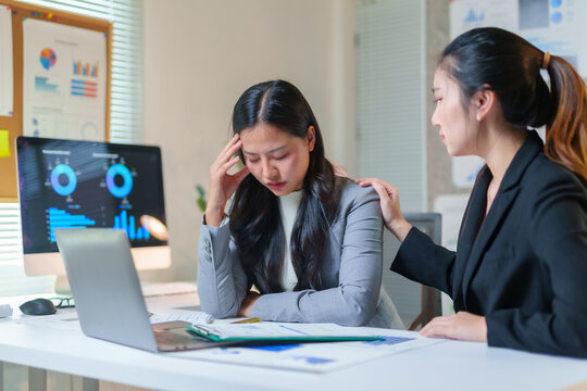 Businesswoman providing comfort to her stressed colleague dealing with a headache in a modern office environment, showcasing empathy and support