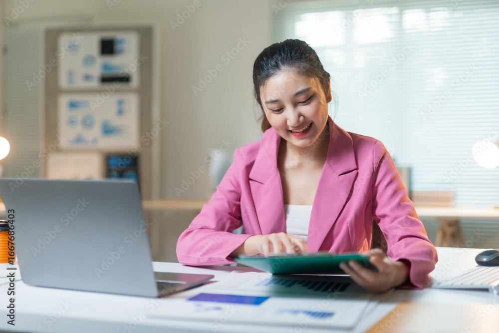 Poster young manager analyzing graphs and working with digital tablet and laptop at her desk in a modern of
