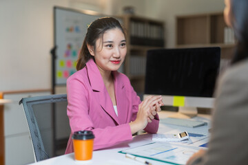 Asian businesswoman discussing with colleague in office meeting, smiling and clasping hands,...