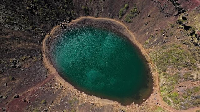 Kerid crater caldera in Iceland drone aerial footage. Stunning 4K view of turquoise water surrounded by red volcanic formations.
