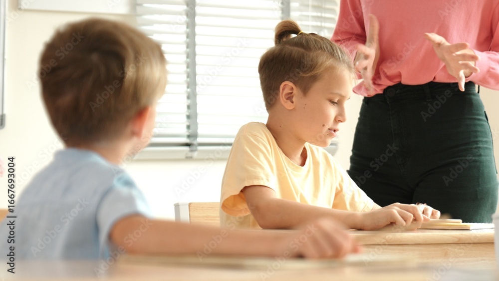 Poster beautiful teacher explaining test while caucasian boy doing classwork and listening explanation. cut