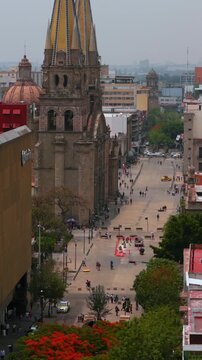Vertical aerial overlooking Av Fray Alcalde in city center, pan right to reveal Guadalajara cathedral facade and twin spires, Mexico