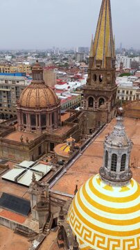 Slow vertical dolly in over Guadalajara Cathedral rooftop, showing yellow striped dome, terracotta domes, and tall spire in Guadalajara Centro