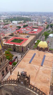 Overhead view of Guadalajara Cathedral&rsquo;s front facade, twin spires, yellow striped dome, and adjacent historic buildings near Plaza de la Liberaci&oacute;n