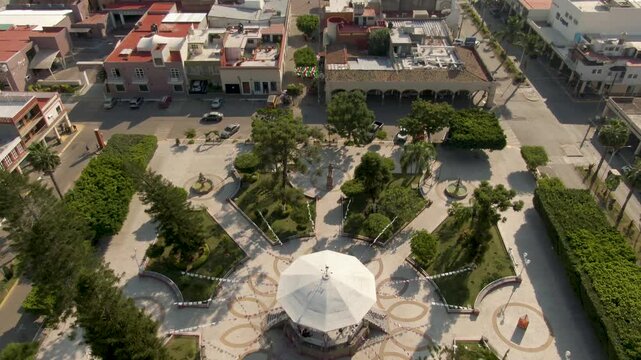 Aerial top-down view of central park with white gazebo, tilt up reveals main church and public market in a small Mexican town