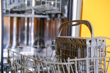 Open built-in dishwasher machine with empty space in modern yellow kitchen. Front view, vertical.