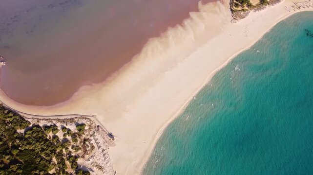 Top-down aerial view of a pink lagoon and turquoise ea separated by a beach.