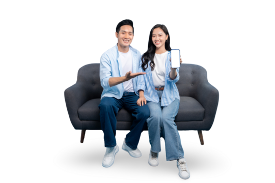 A happy couple is sitting on a couch while pointing to a mobile phone in a light background. They are smiling and expressing content with their appearance.