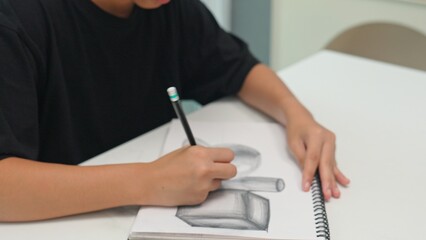 Student practicing pencil drawing of 3D geometric shapes in sketchbook