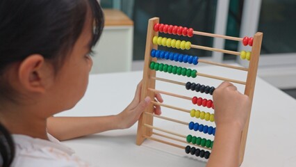 Young girl studying and writing homework with abacus on desk