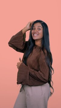 Stylish woman making a kissy face and thumbs up gesture, showing confidence and playfulness against a peach background 