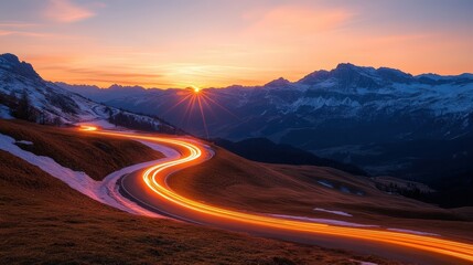 Stunning mountain landscape du sunset with winding illuminated road and snow capped peaks in the background