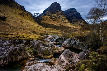 River Coe flows through Glen Coe with The Three Sisters mountains in early spring, Scotland