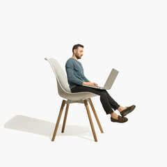 A man sits on an office chair with a huge laptop on his lap.