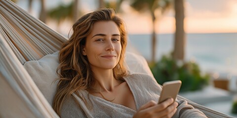 Young caucasian female relaxing in hammock using smartphone at tropical beach
