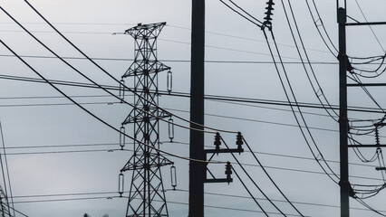 Power Grid Network: Overhead power lines and a towering transmission tower stand under a cloudy...