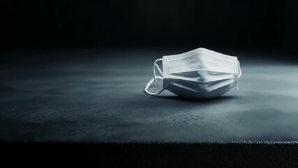 Discarded white surgical mask lying on dark gray background, representing healthcare protection during viral pandemic period - Powered by Adobe