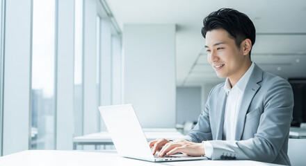 オフィスでパソコン作業をする笑顔の若いビジネスマン