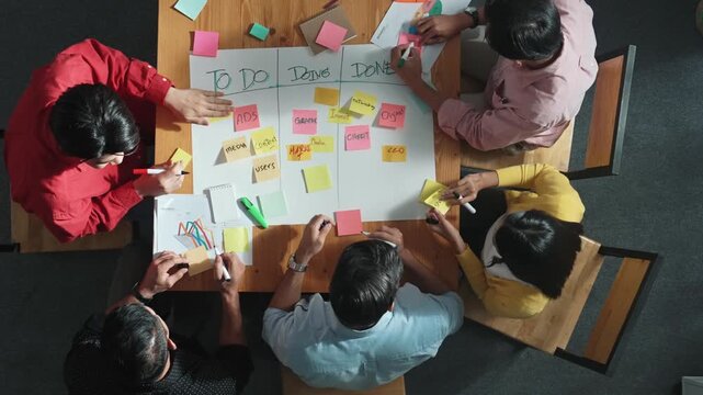 Top view of people writing and making scrum task board while writing marketing and planning strategy at colorful sticky notes. Smart team manage work performance by using kanaban board. Convocation.
