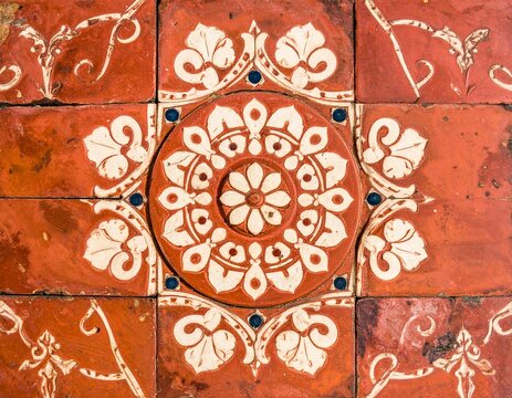 Weathered Athangudi tile in brick-red terracotta with motif detail, worn edges and faded pigments, authentic handmade texture