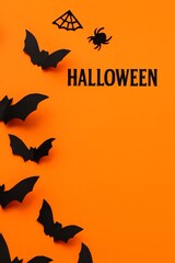 Fototapeta premium Black bats and spider decorations on vibrant orange background create a festive Halloween atmosphere, showcasing playful elements for seasonal celebrations and themed events