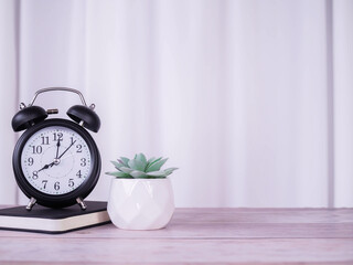 Creative desk, Black alarm on hardcover book and cactus with white curtain for background. Copy...