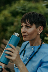 Female doctor drinking from reusable water bottle during break in park