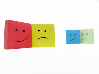 a happy red sticky note with a sad yellow sticky note, while two other sticky notes with unhappy faces are out of focus in the background. concept of a person supporting someone who is bullied