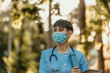 Female doctor wearing protective mask walking in park during coronavirus pandemic