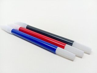 shot of three markers—black, red, and blue—lying diagonally side by side on a clean white...