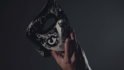 Caucasian man hand holding a venetian mask with black and white decorations on dark background