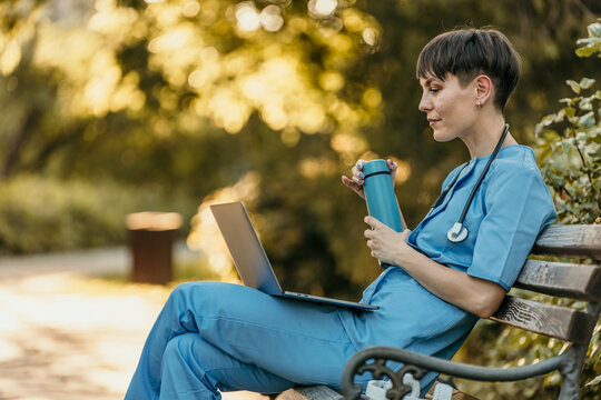 Female doctor working with laptop and drinking coffee in park during break time