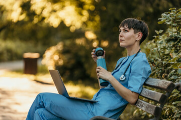 Doctor relaxing on bench with laptop and water bottle after work in park