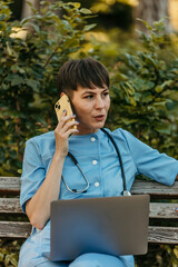 Female doctor talking on phone and working on laptop in park