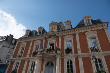 Cauteret's town hall building features elegant architecture with colorful flowers adorning the balconies, set against a backdrop of a brilliant blue sky and majestic mountains.