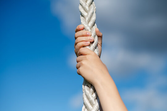 Children’s hands gripping sports rope at outdoor playground against blue sky