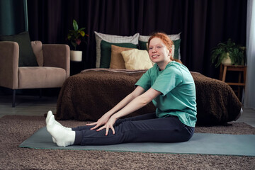 Young girl practicing yoga at home on a mat in a cozy bedroom in the afternoon