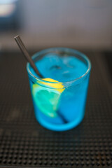 A Refreshing Blue Cocktail Served in a Glass with a Lemon Wedge and a Straw on a Dark Countertop Perfect for a Summer Party or Special Occasion