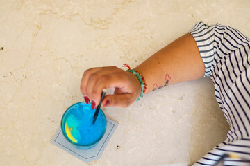 Vibrant Blue Cocktail Being Stirred with a Spoon by a Hand with Bracelets on a Textured Surface