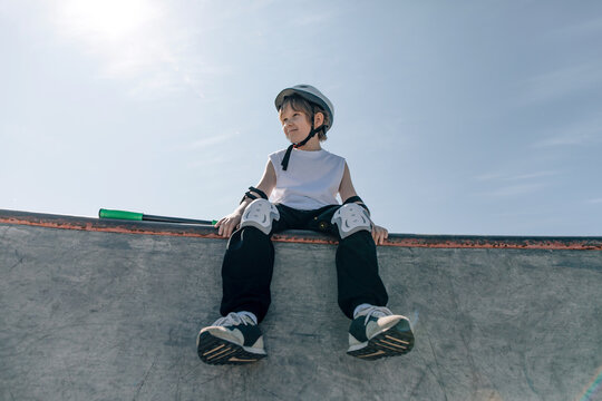 Happy boy with scooter in safety gear at skatepark, close-up