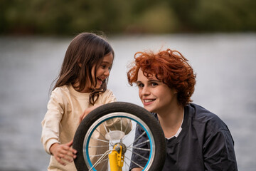 Mother and little daughter play with a bicycle wheel during a walk.