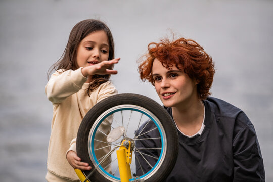 Mother and little daughter play with a bicycle wheel during a walk.