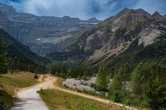 A picturesque hiking trail leads through lush greenery under towering mountains in Cirque de Gavarnie, a breathtaking destination in the Pyrenees showcasing stunning natural landscapes.