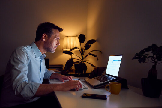 Businessman working late at home with laptop highlighting overtime hustle