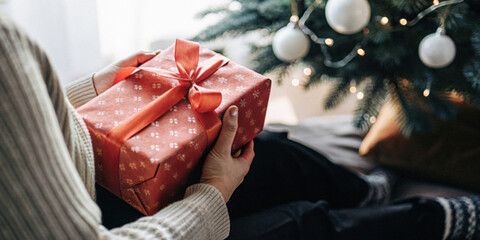 Festival background. Person hand holding a Christmas gift beside a Christmas tree in a catmosphere...
