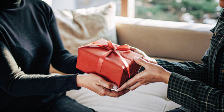 Festival background. Hands of two people exchanging a red gift box in the idea of giving gifts to your loved ones during the Christmas and New Year festivities
