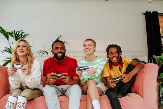 Multiracial friends playing video game sitting on sofa at home