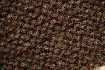 Dark brown wool knitted fabric texture, macro. Close-up view of warm, fuzzy wool yarn in a dense hand-knitted pattern. Natural textile structure with visible fibers and stitches