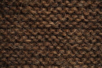 Dark brown wool knitted fabric texture, macro. Close-up view of warm, fuzzy wool yarn in a dense hand-knitted pattern. Natural textile structure with visible fibers and stitches