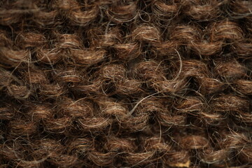 Dark brown wool knitted fabric texture, macro. Close-up view of warm, fuzzy wool yarn in a dense hand-knitted pattern. Natural textile structure with visible fibers and stitches